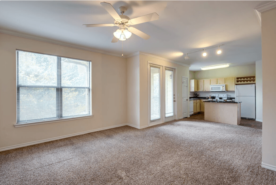 an empty living room with a ceiling fan and a kitchen