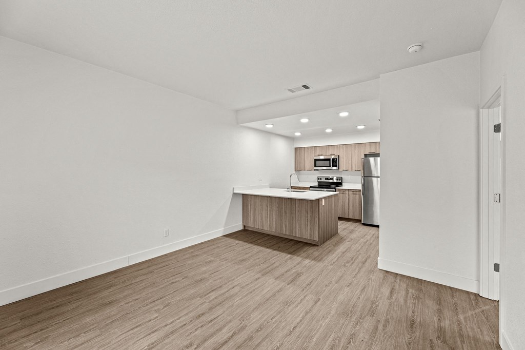 the living room and kitchen of an apartment with white walls and wood flooring