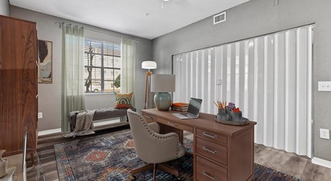 A room with a desk, chair, and a window with curtains.