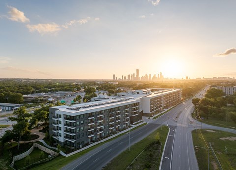 A modern apartment building is situated on a road with a city skyline in the background.