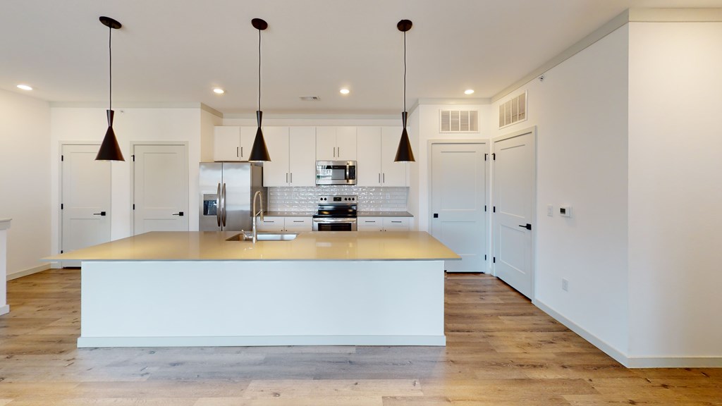 A kitchen with a white island and pendant lights.