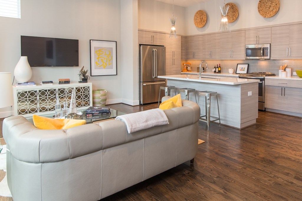 A modern living room with a grey sofa and a kitchen in the background.