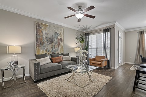 A living room with a grey couch, a glass coffee table, and a large painting on the wall.