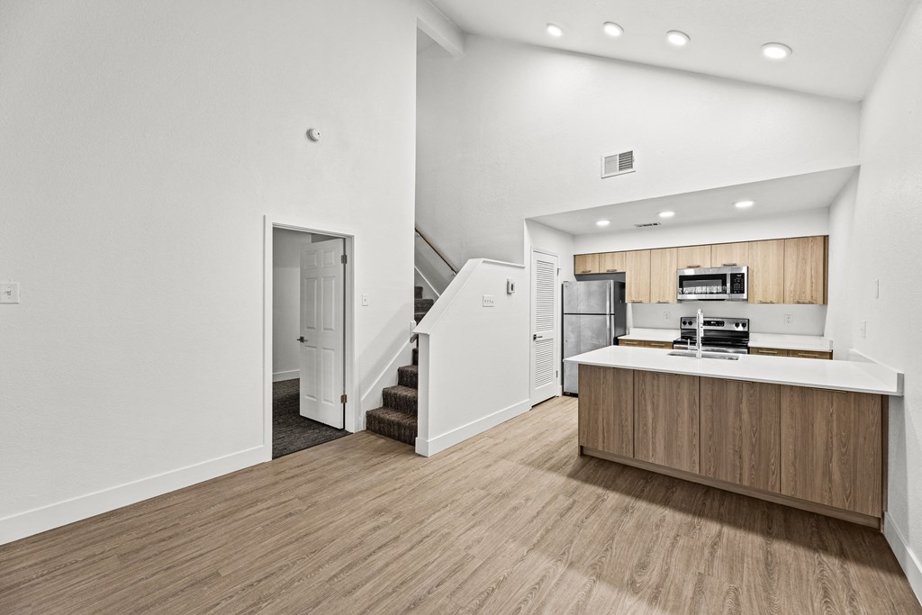 the living room and kitchen of an apartment with white walls and wood flooring