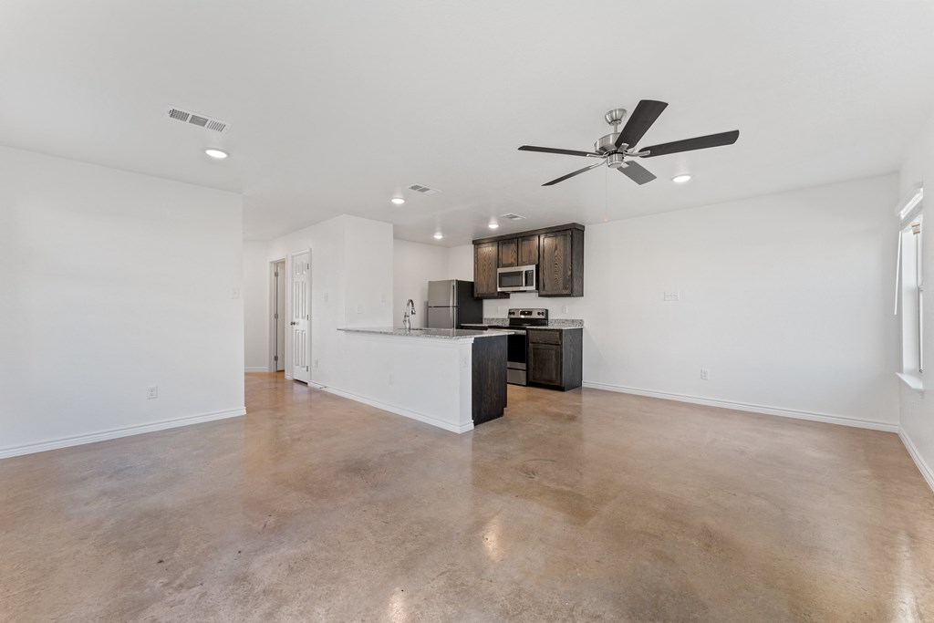 an empty living room with a kitchen and a ceiling fan