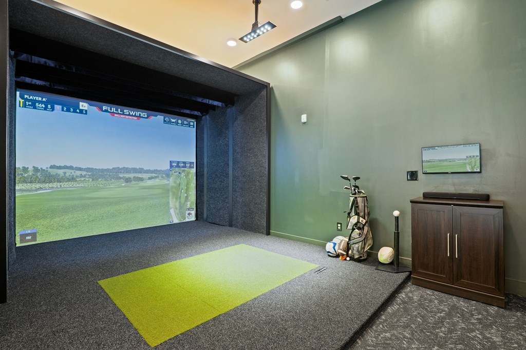A room with a golf simulator and a yellow mat on the floor.