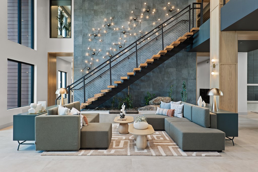 A lobby room with a grey sofa, a coffee table, and a staircase with lights.