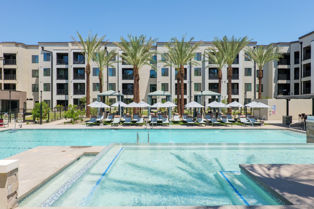 A pool surrounded by palm trees and lounge chairs in front of a building.
