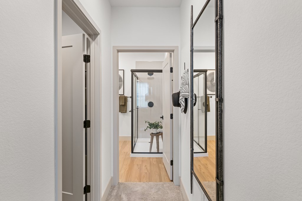 A hallway with a mirror on the wall and a door on the left.