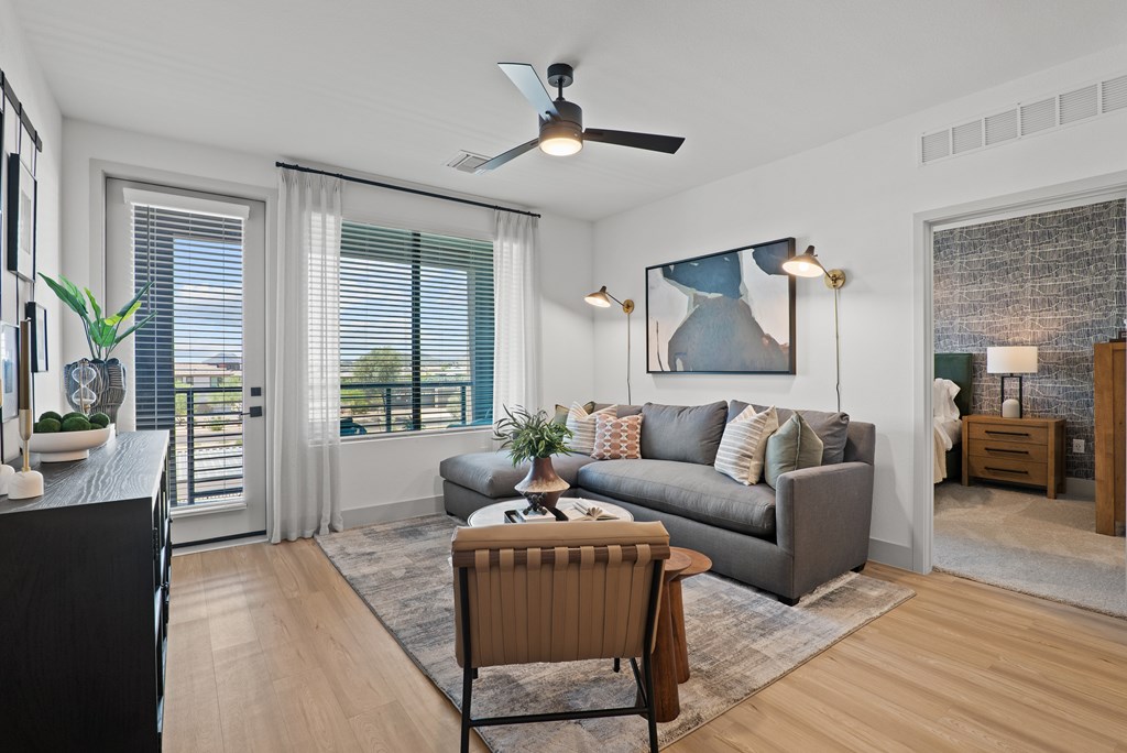 A living room with a grey couch, a brown armchair, and a ceiling fan.