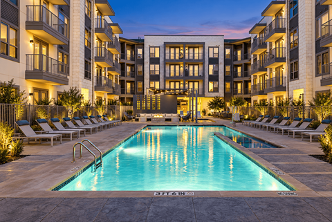 A swimming pool in front of a building with lounge chairs around it.