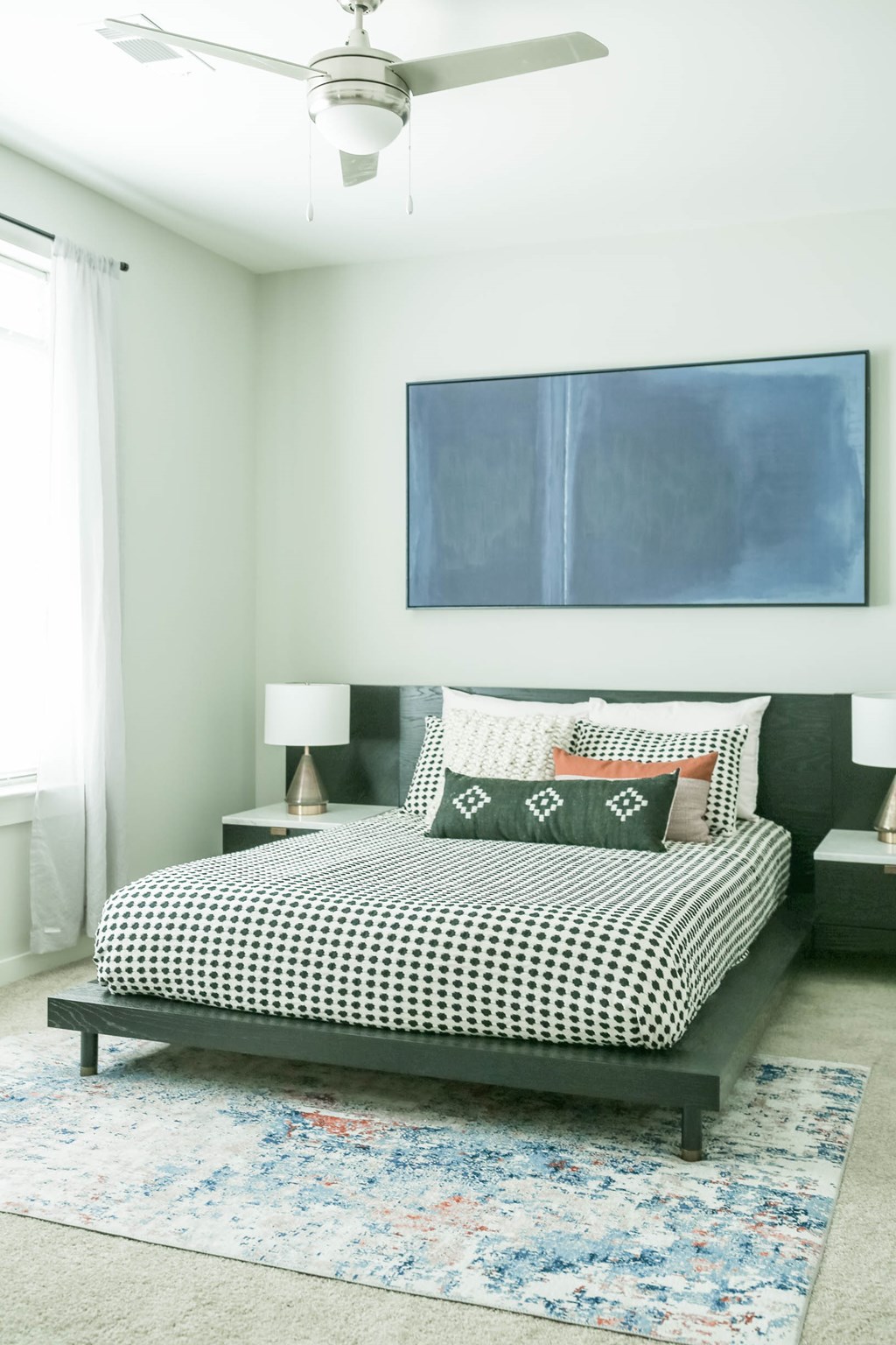 A bedroom with a bed, a ceiling fan, and a painting on the wall.