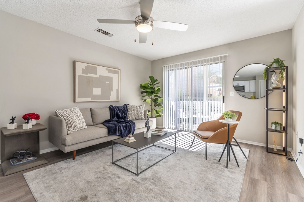 A living room with a grey couch, a glass coffee table, and a ceiling fan.