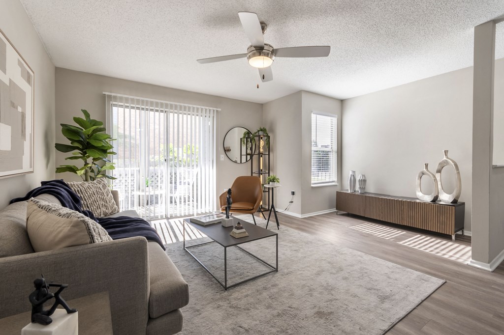 A living room with a grey couch, a glass coffee table, and a ceiling fan.