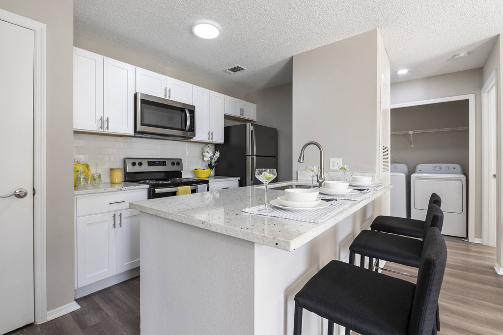 A kitchen with a white countertop and black chairs.