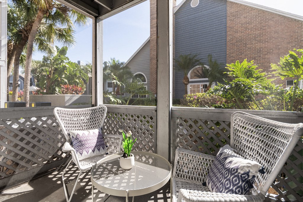 A patio with two chairs and a table with a vase of flowers on it.