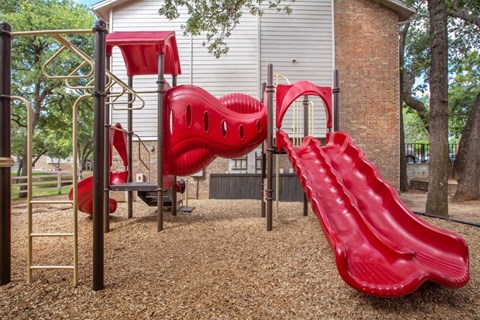 A red slide and climbing structure in a playground.