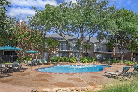 A pool surrounded by chairs and trees in front of a house.