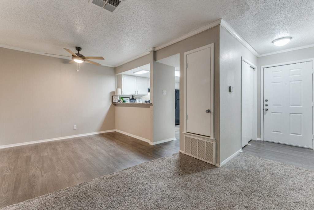 an empty living room with a ceiling fan and a kitchen in the background