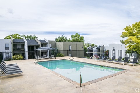 A swimming pool surrounded by a black fence and a few chairs.