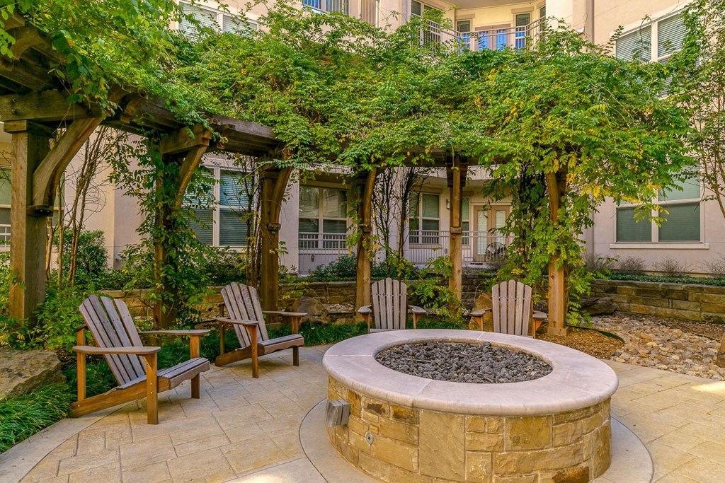 a fire pit with two chairs and a pergola in front of a building