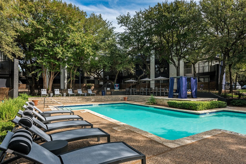 a swimming pool with chaise lounge chairs and trees in the background