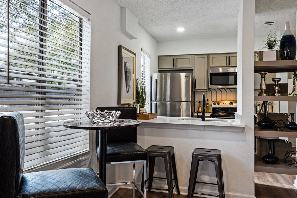 a kitchen with a breakfast bar and stools next to a large window with blinds