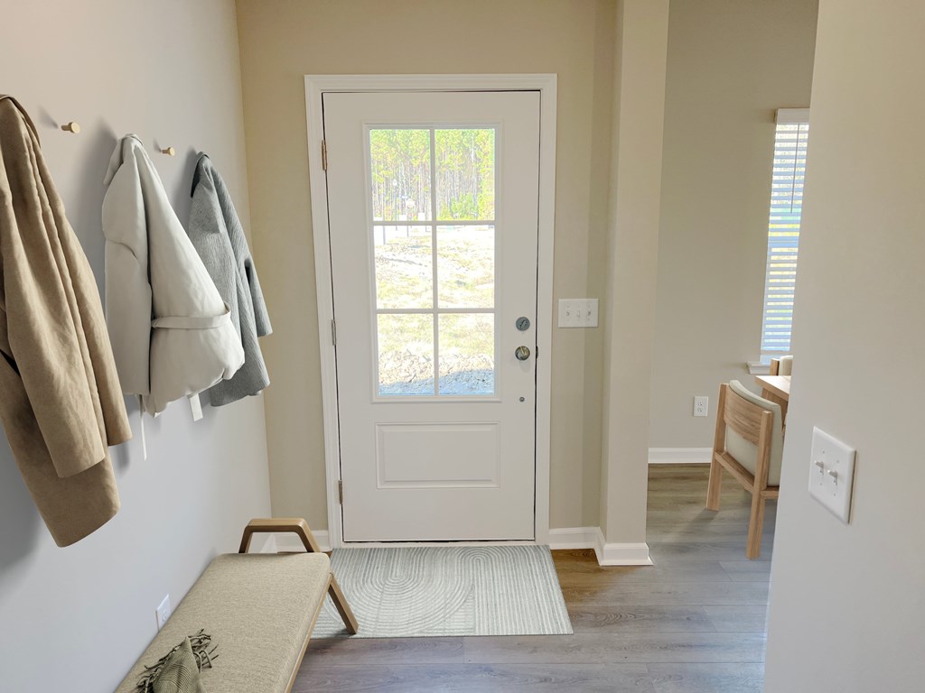 A white door is in the middle of a hallway with a bench and coat hooks on the wall.
