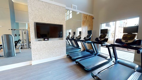 A gym with treadmills and a television mounted on the wall.
