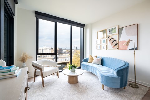 A blue couch sits in a living room with a large window overlooking the city.