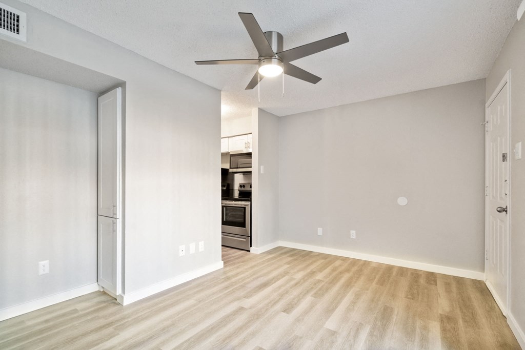 an empty living room with a ceiling fan and a kitchen