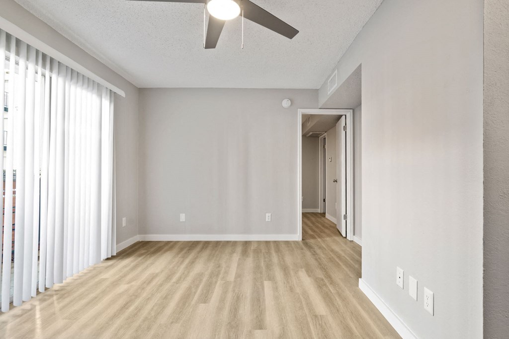 an empty living room with a large window and a ceiling fan