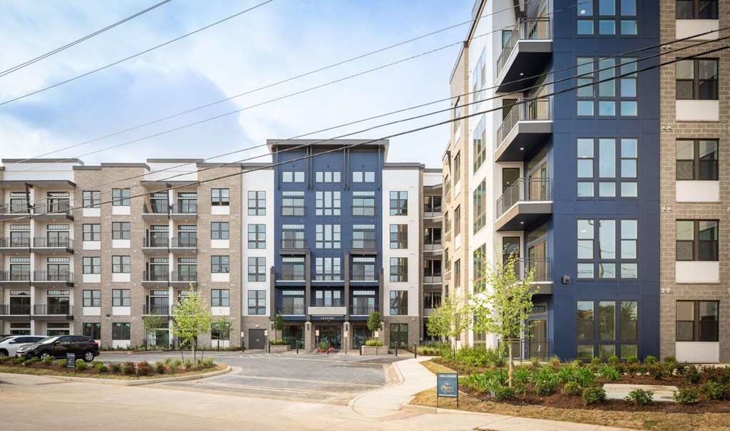 A row of modern apartment buildings with a parking lot in front.