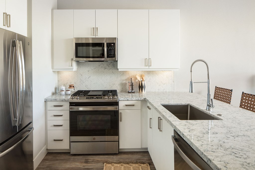 a white kitchen with stainless steel appliances and marble counter tops