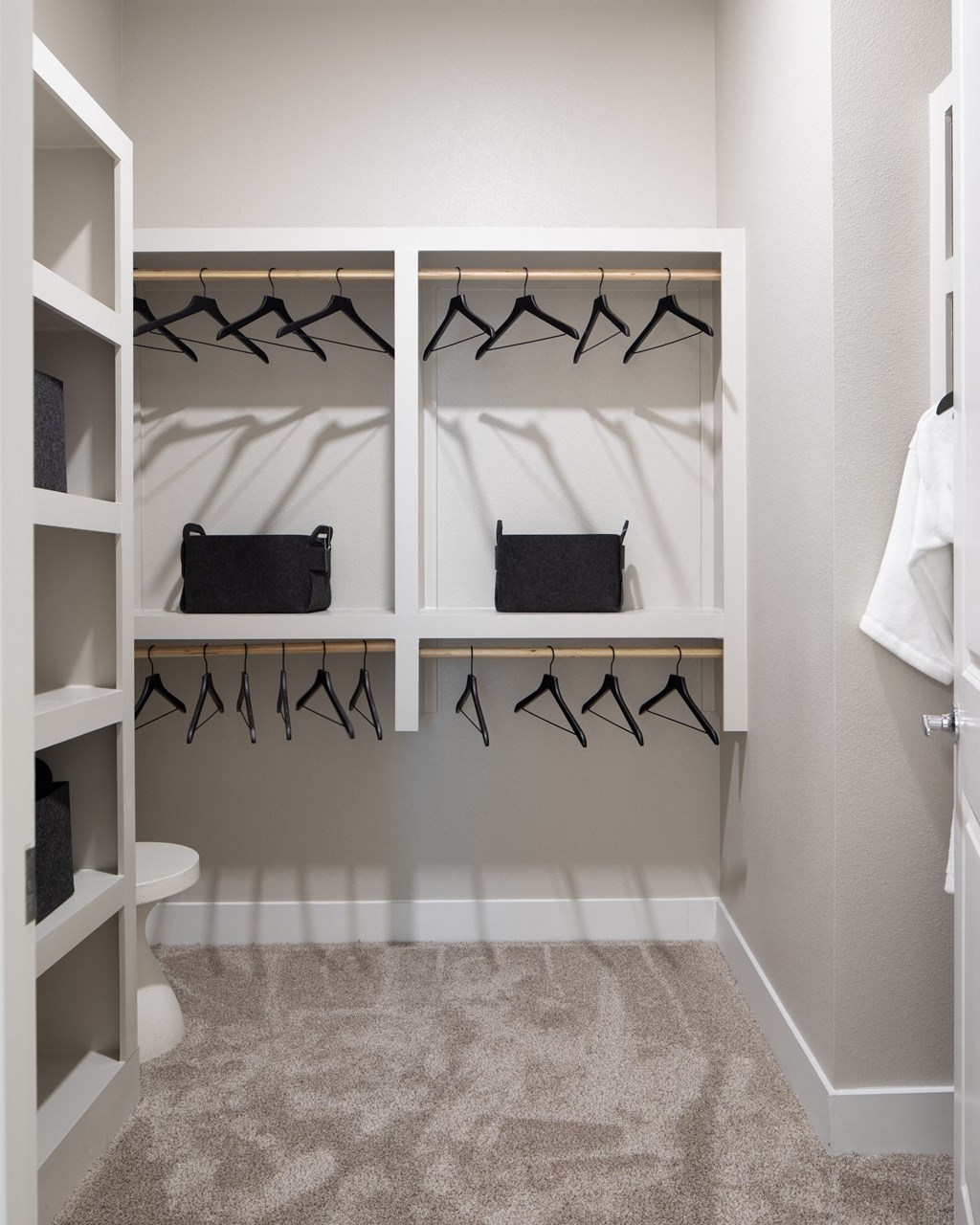 a walk in closet in a master bathroom with white shelves and black hangers