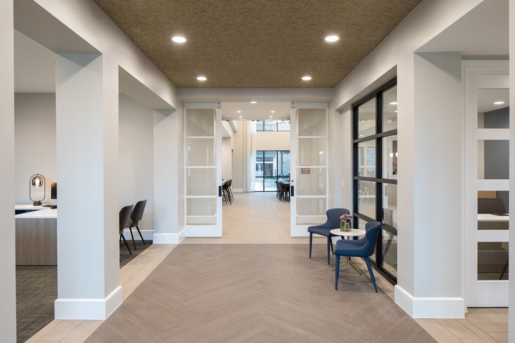 a communal area with chairs and tables and a hallway with glass doors