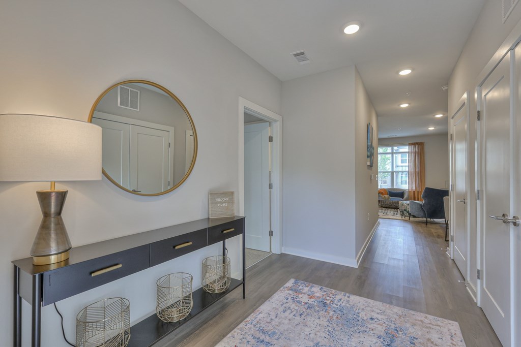 A hallway with a round mirror and a lamp on a console table.