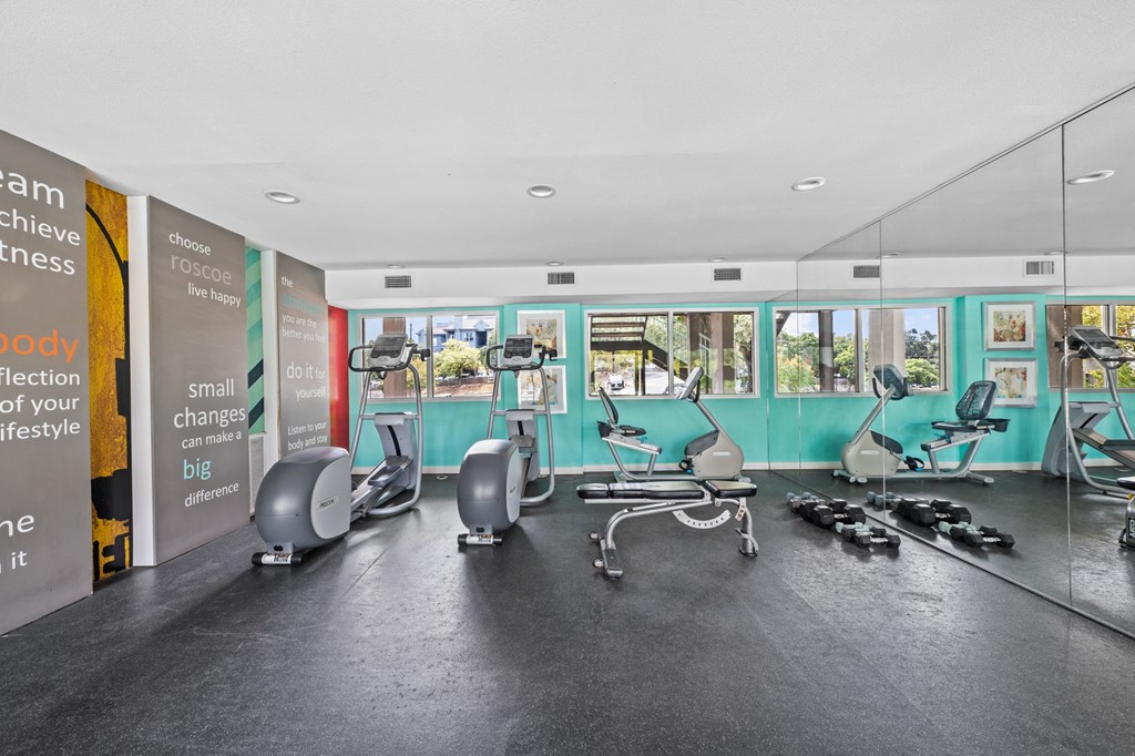 a gym with exercise machines and chairs in a large room with windows