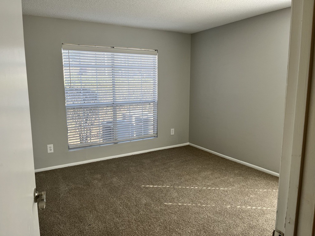 an empty room with a large window and carpeting
