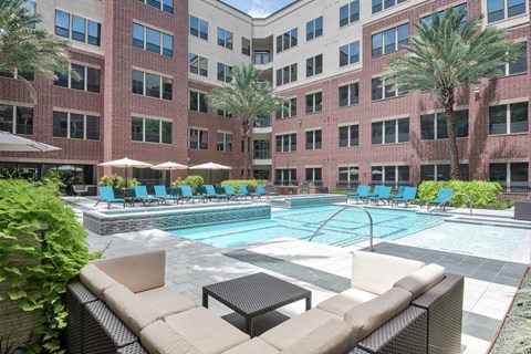 A large pool surrounded by chairs and umbrellas in front of a brick building.