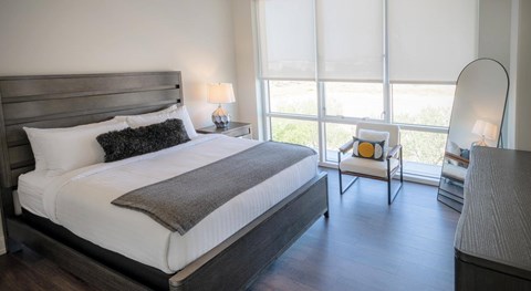 A bedroom with a large bed and a chair by the window.