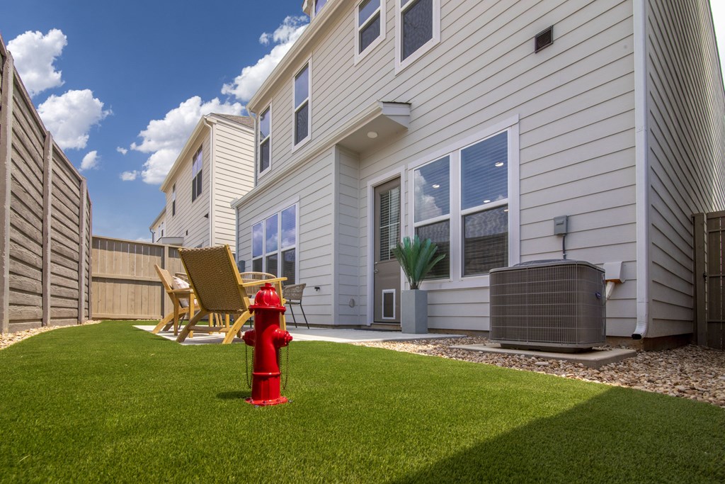 A red fire hydrant sits on a green lawn in front of a white house.