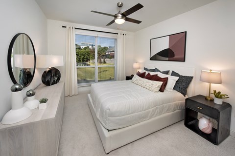 A bedroom with a large bed, a mirror, and a ceiling fan.