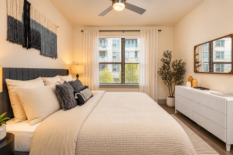 A bedroom with a large bed, a ceiling fan, and a window with blinds.