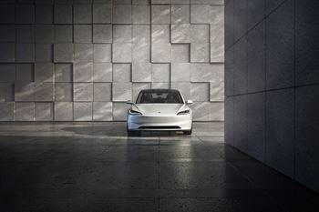 A white car is parked in front of a wall with a geometric pattern.