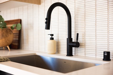 A modern kitchen sink with a black faucet and a white countertop.