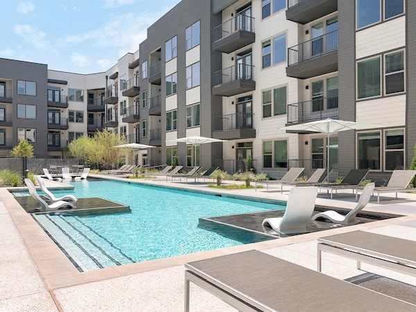 a swimming pool with lounge chairs and umbrellas in front of an apartment building