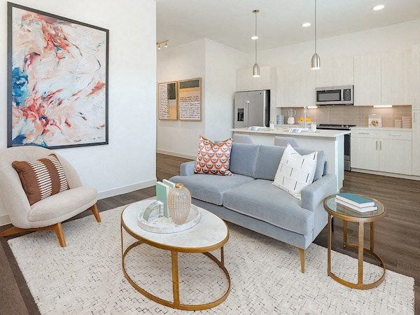 a living room with a couch table and chairs and a kitchen in the background