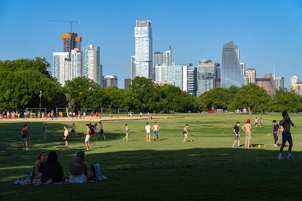 a group of people playing frisbee in a park with a city skyline in the background