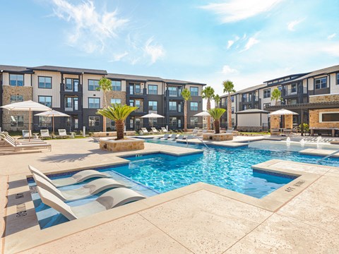 A swimming pool surrounded by lounge chairs and umbrellas in front of a multi-story apartment building.